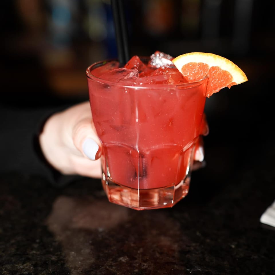 A hand holds a vibrant red cocktail with ice and a grapefruit slice at Galloway Diner.