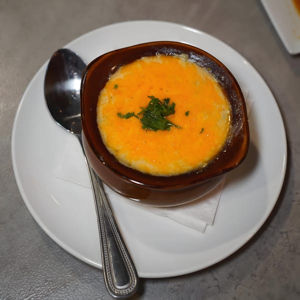A brown bowl of baked macaroni and cheese, topped with melted cheddar and parsley, on a white plate.