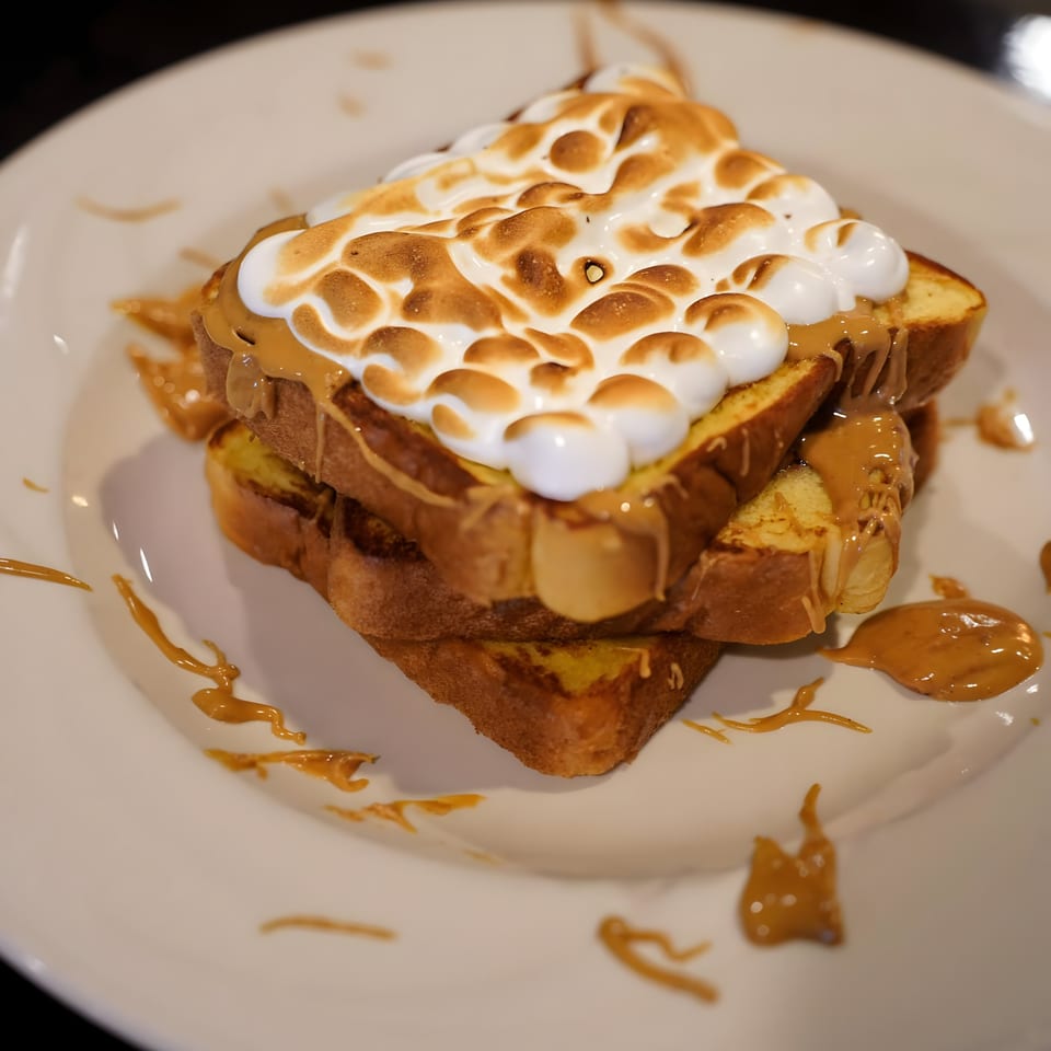 Peanut butter and toasted marshmallow French toast on a white plate with peanut butter drizzle.