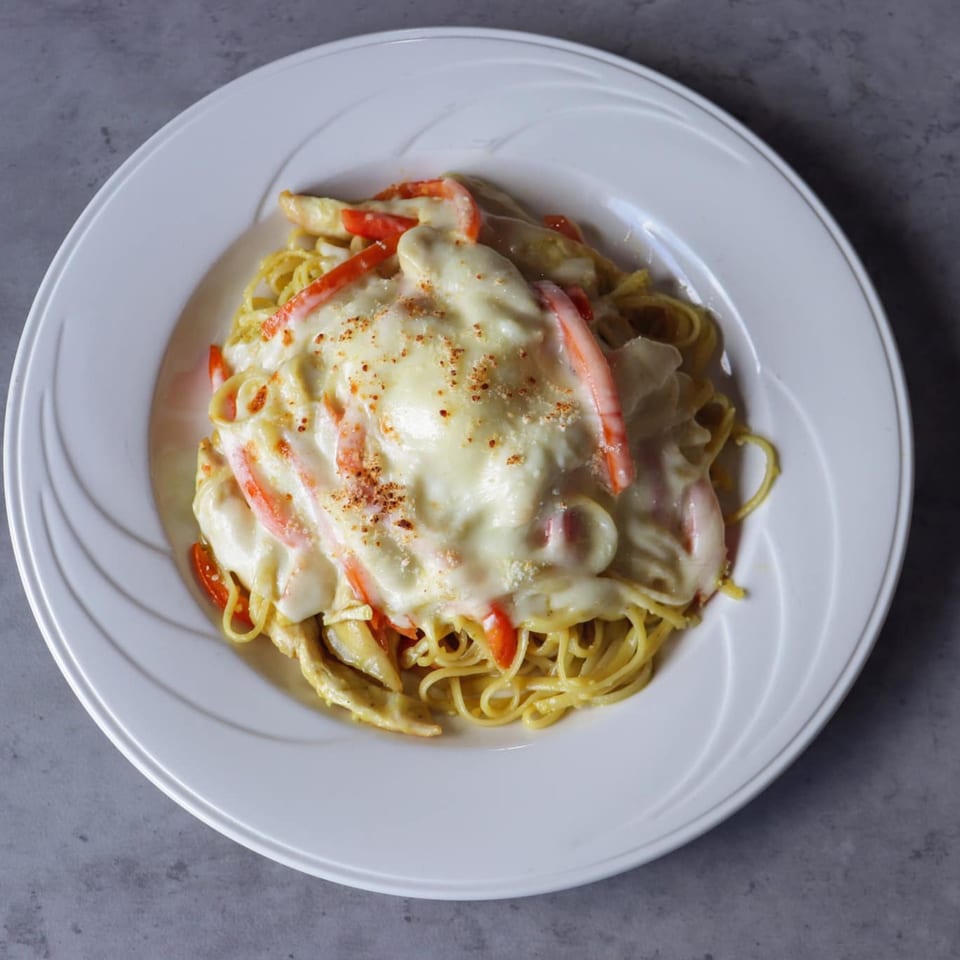 Creamy pasta dish with red bell peppers and chicken, topped with cheese and spices.