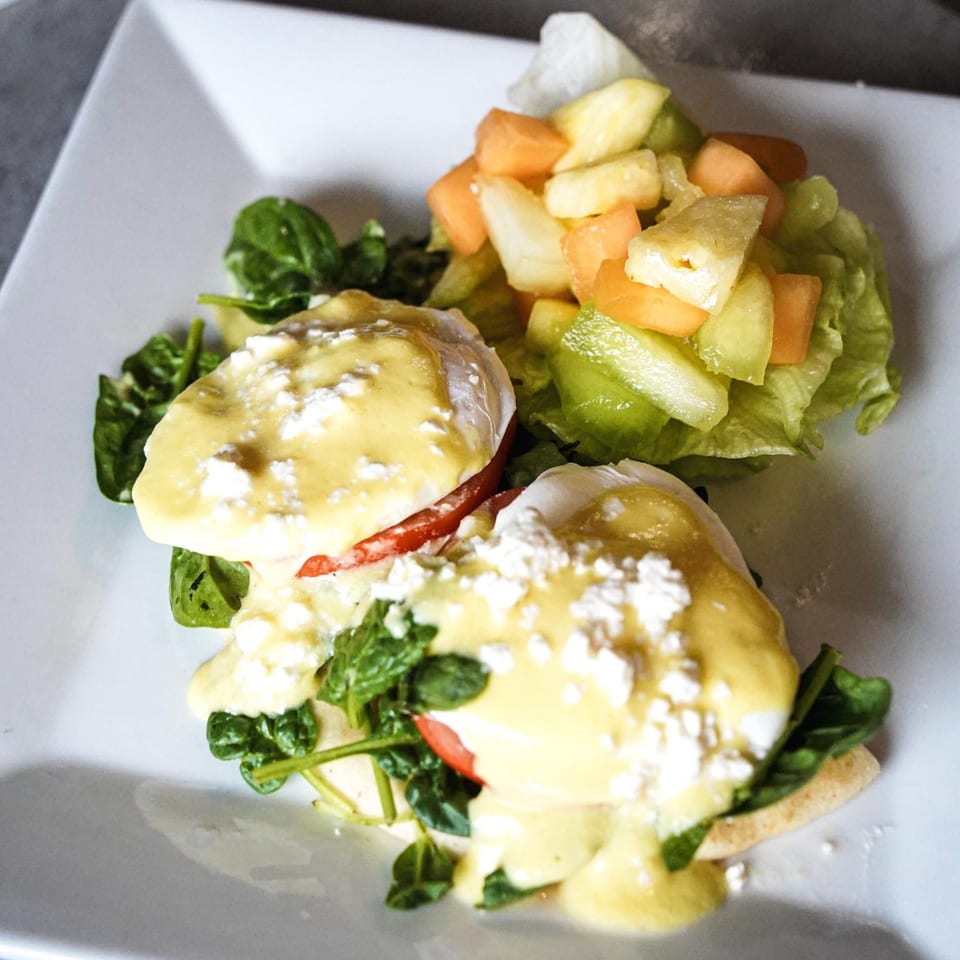 Eggs Benedict with spinach, tomato, hollandaise, feta, and a side of fruit salad.