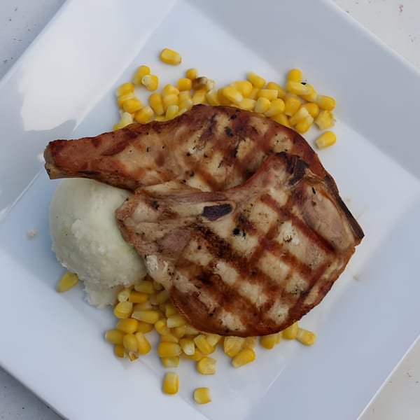 Two grilled pork chops with mashed potatoes and corn on a white plate at Galloway Diner.