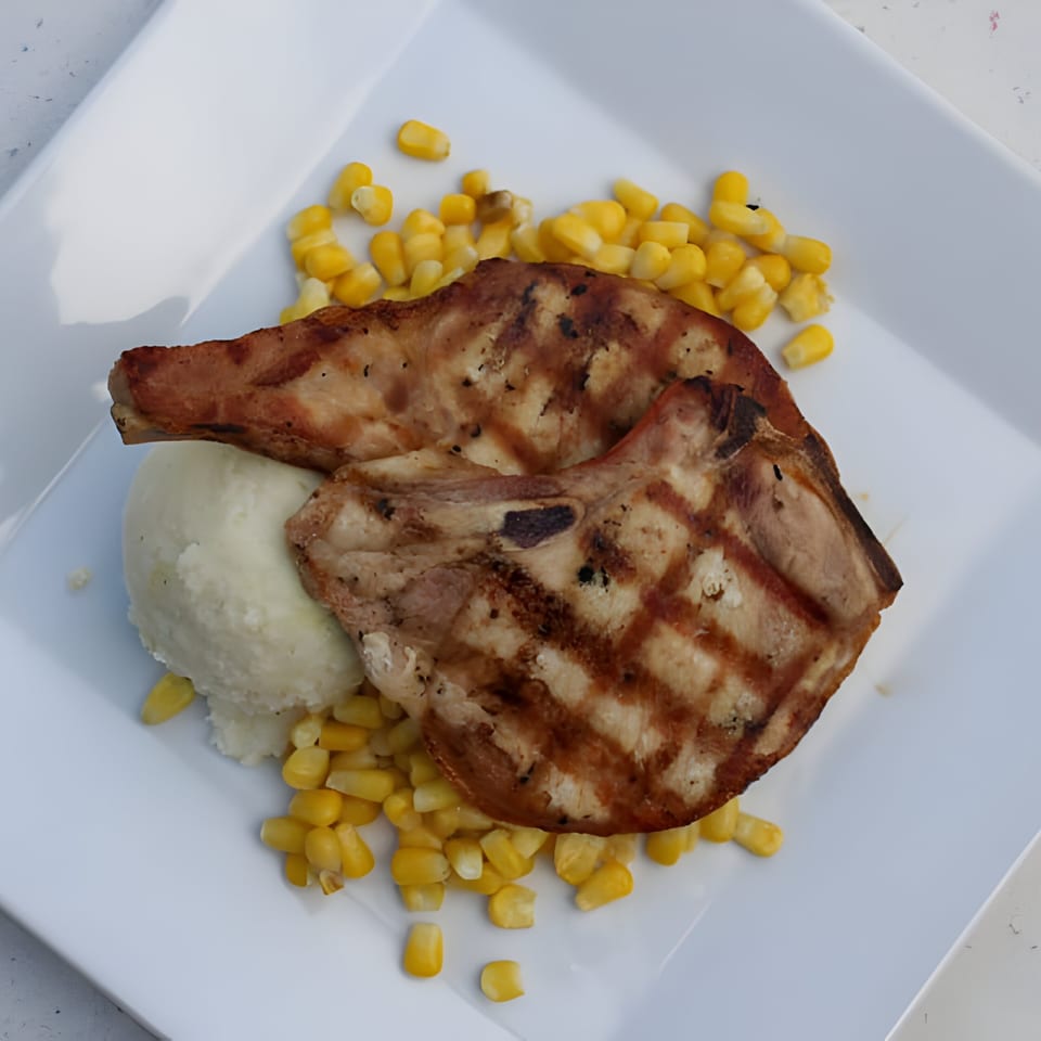 Two grilled pork chops with mashed potatoes and corn on a white plate at Galloway Diner.